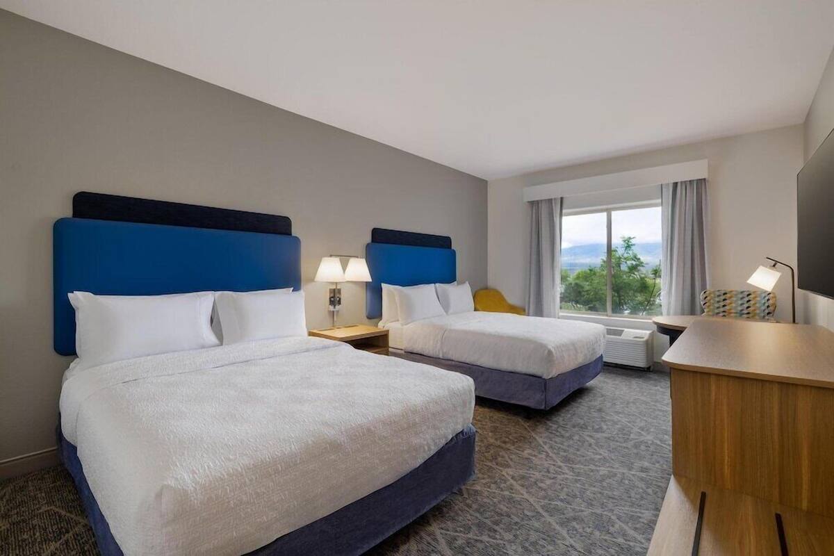 A hotel room with two beds, a desk, a chair, a TV, and a window with a view.