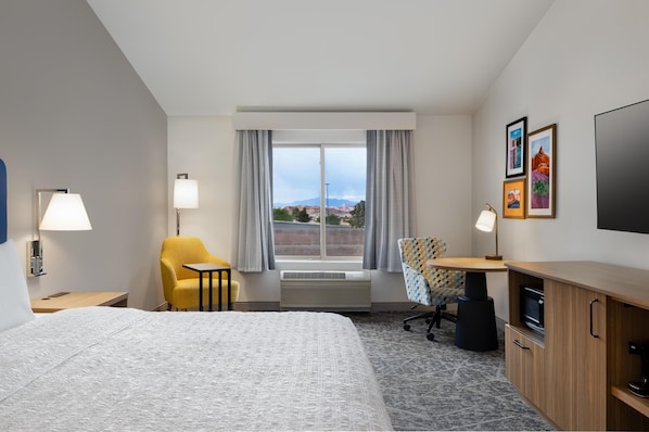 A hotel room with a bed, a desk, a chair, a TV, and a window with a view of mountains.