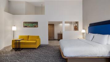 Een hotelkamer met een bed, een gele bank, een kleine tafel en een schilderij aan de muur.