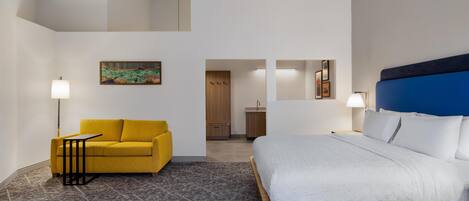 Una habitación de hotel con una cama, un sofá amarillo, una mesita y un cuadro en la pared.