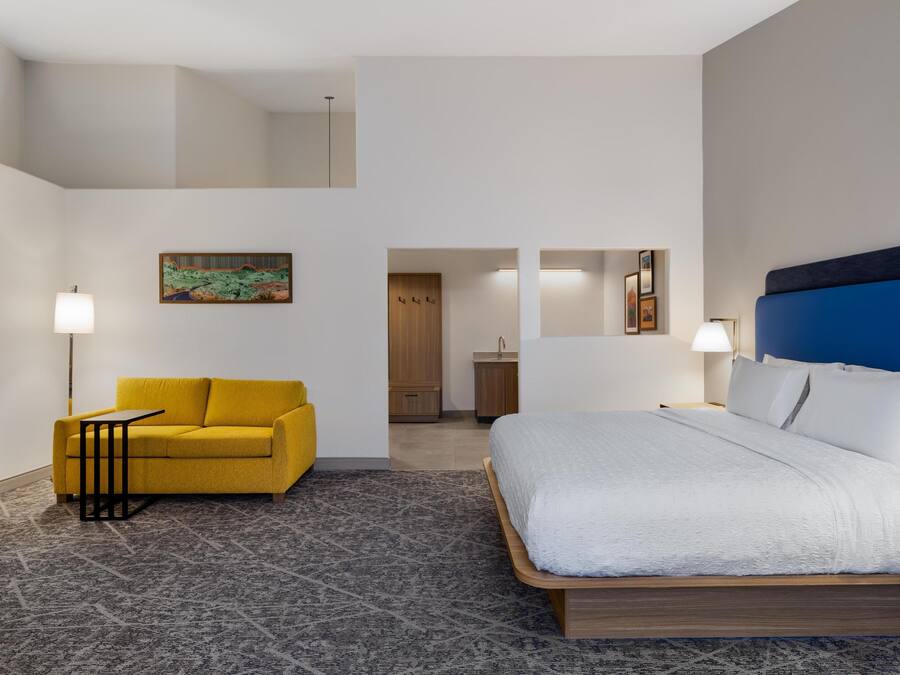 Een hotelkamer met een bed, een gele bank, een kleine tafel en een schilderij aan de muur.