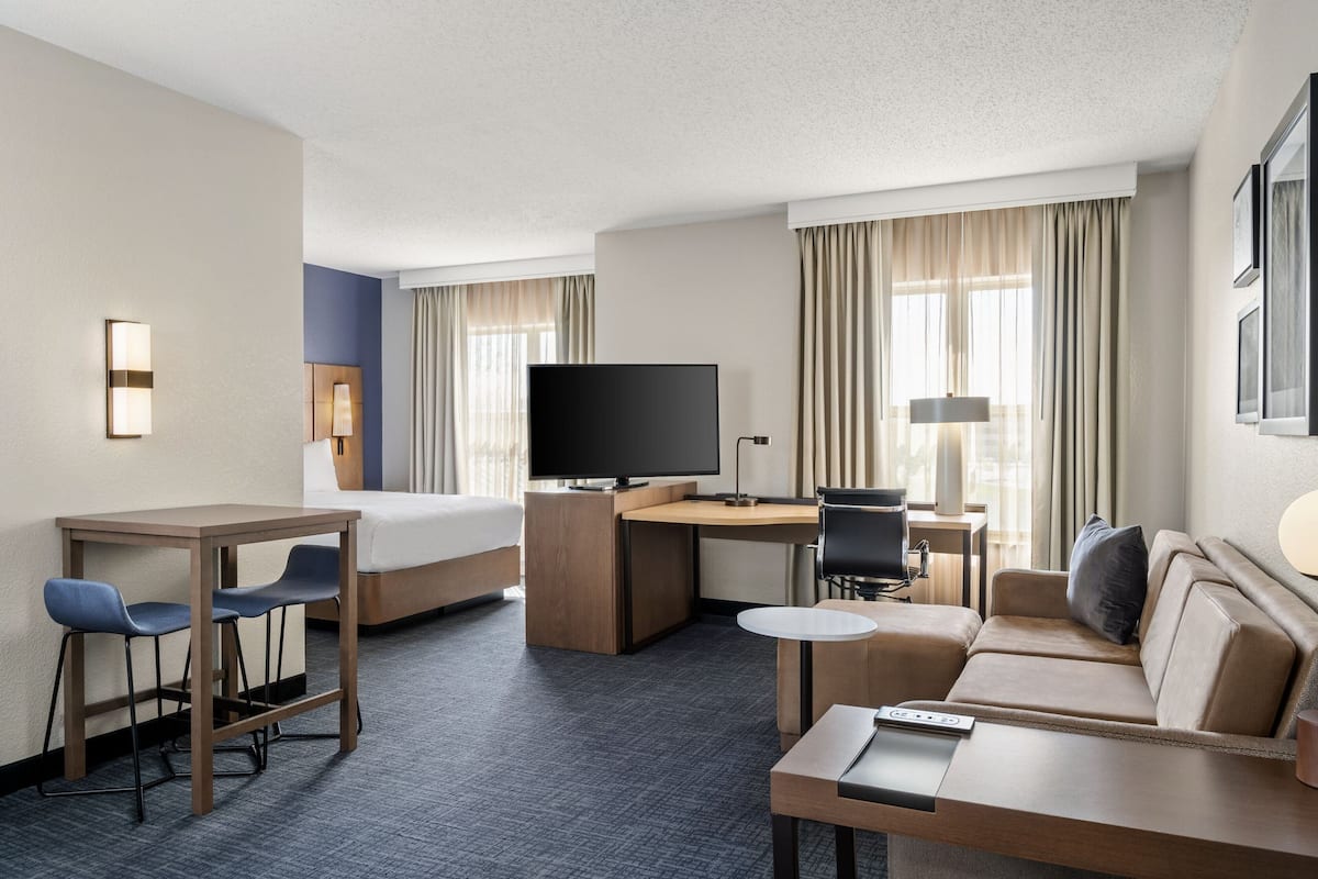 A hotel room with a bed, desk, television, seating area, and a small table.