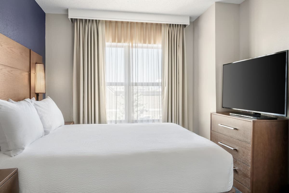 A hotel room with a large bed, a TV on a wooden cabinet, and a window with curtains.