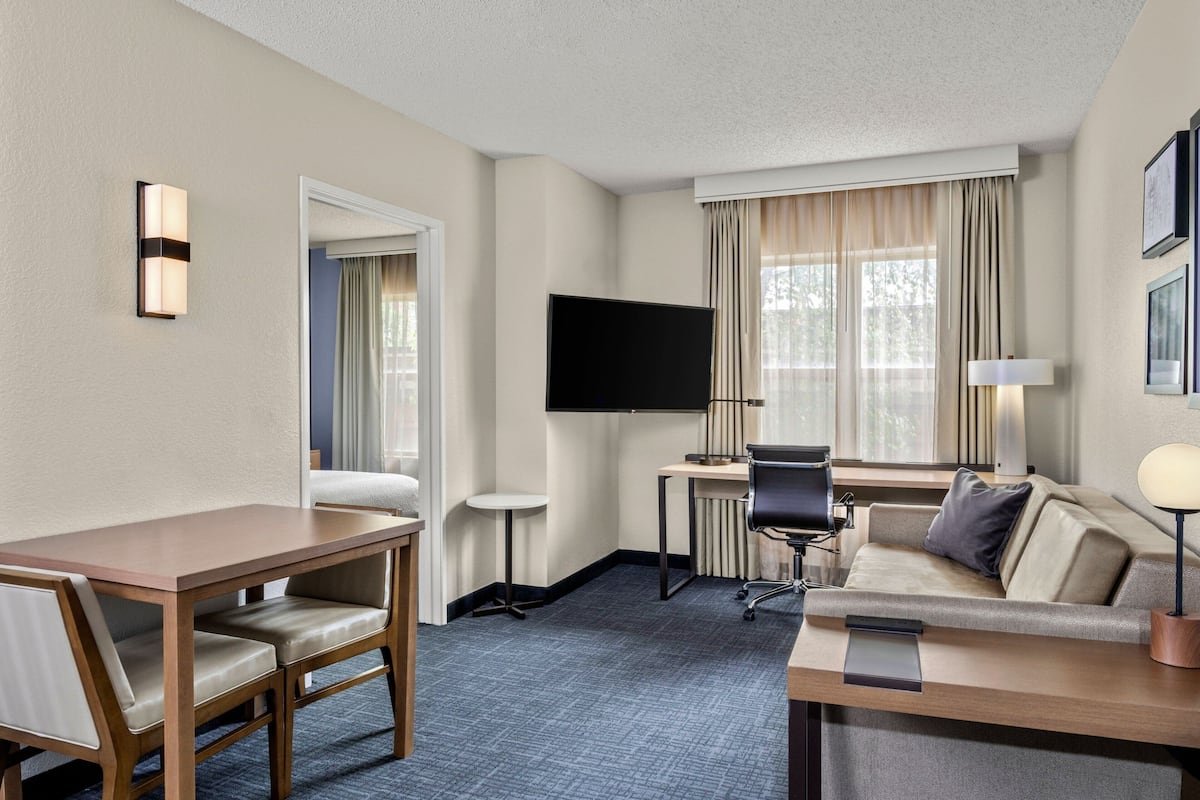A hotel room with a wooden desk, a flat-screen TV, a sofa, and a lamp.
