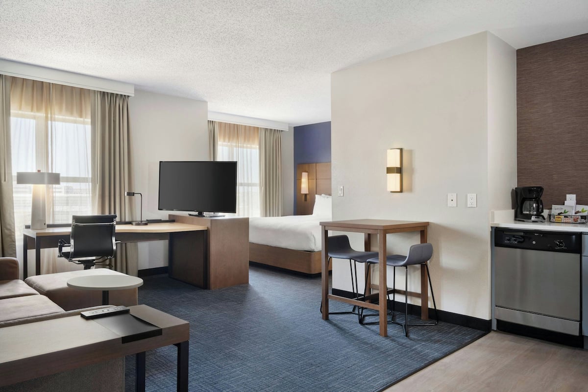 A hotel room with a bed, desk, TV, kitchenette, and seating area.