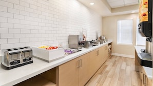 Uma cozinha moderna com azulejos brancos tipo metrô, armários de madeira, uma torradeira, uma fruteira e uma máquina de café.