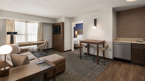 Quarto de hotel com sofá, escrivaninha, mesa de jantar, cozinha compacta e cama.