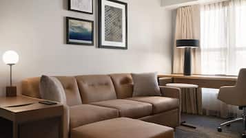 Une chambre d’hôtel moderne avec un canapé en cuir marron, une petite table ronde, une lampe et deux œuvres d’art encadrées accrochées au mur.
