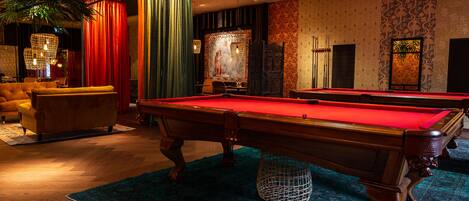 Una sala de billar con dos mesas de pool, un sofá y una pared decorativa con papel tapiz estampado.