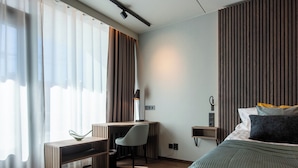 A modern hotel room with a bed, desk, and chair, featuring a view of the city through large windows. - Hotell Arkipelag (Mariehamn)
