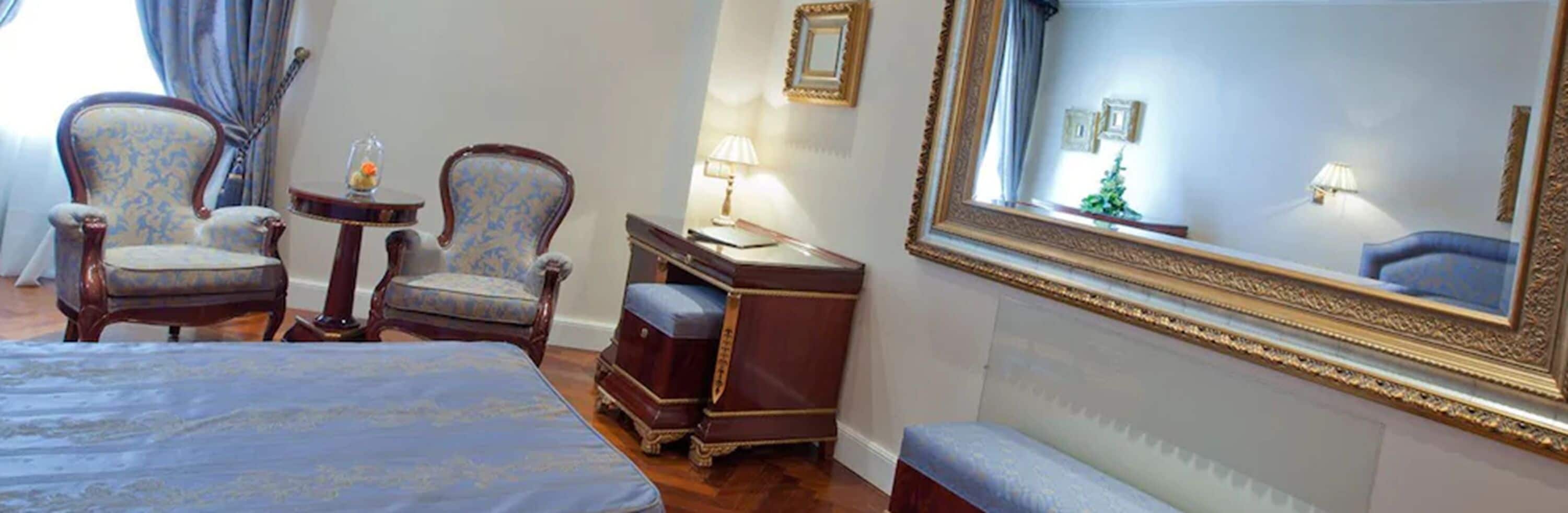 Habitación de hotel con una cama grande, dos sillones, una mesita, un aparador y un espejo amplio.