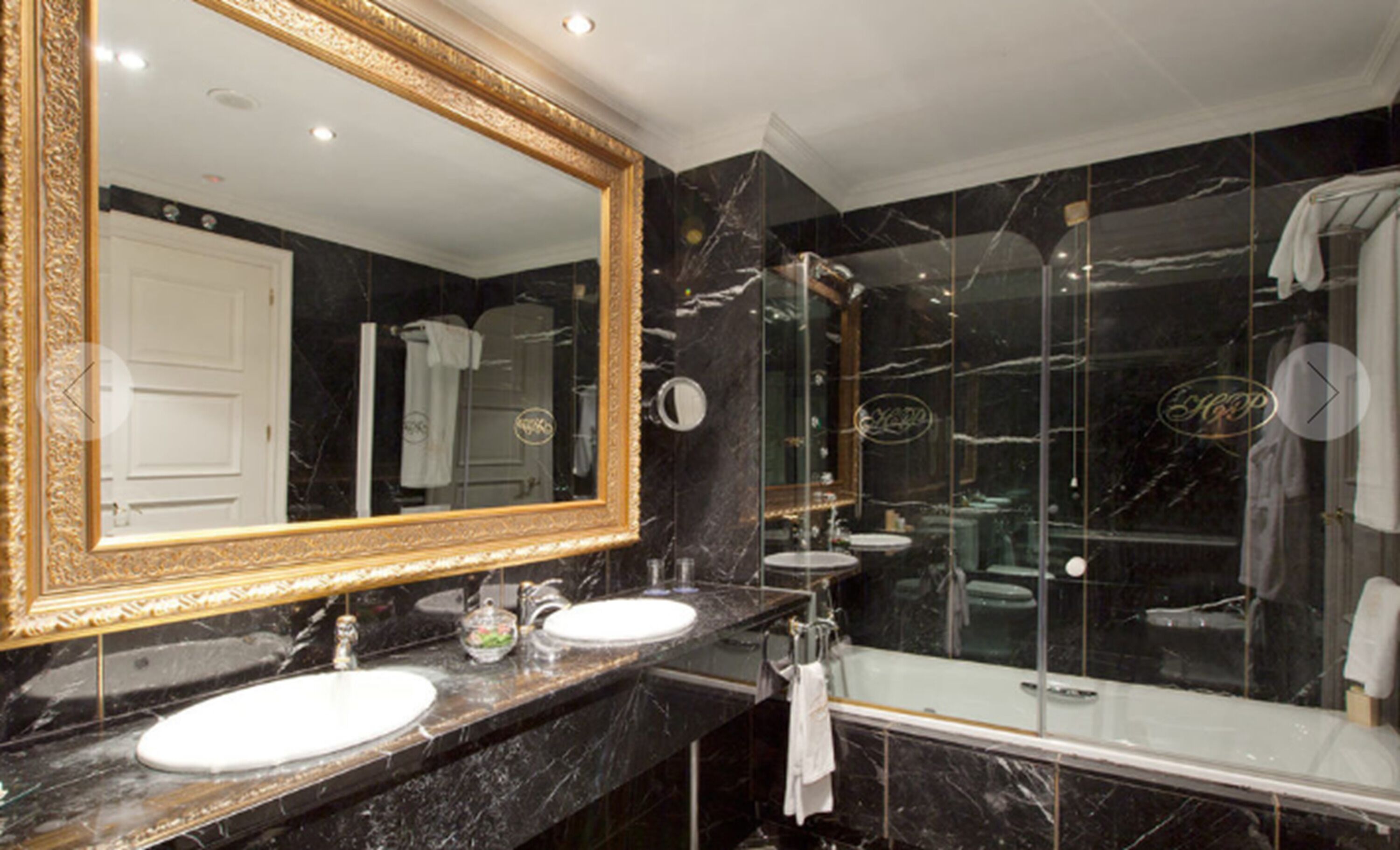 Un baño con dos lavamanos, un espejo grande y una ducha con mampara de vidrio.