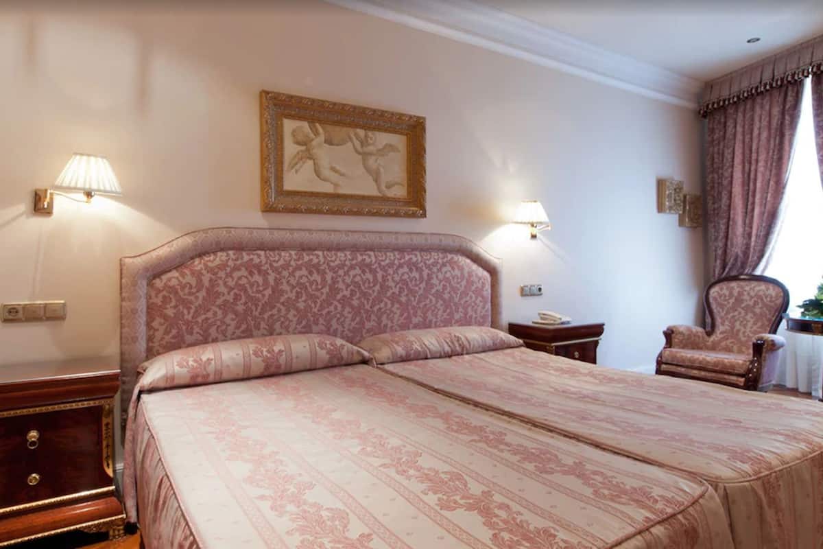 Une chambre avec un grand lit, deux lampes de chevet, une œuvre d’art encadrée au mur, une chaise et une table de chevet.