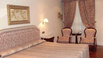 Una habitación de hotel con una cama grande, dos sillones, una mesita pequeña y una lámpara de pared.