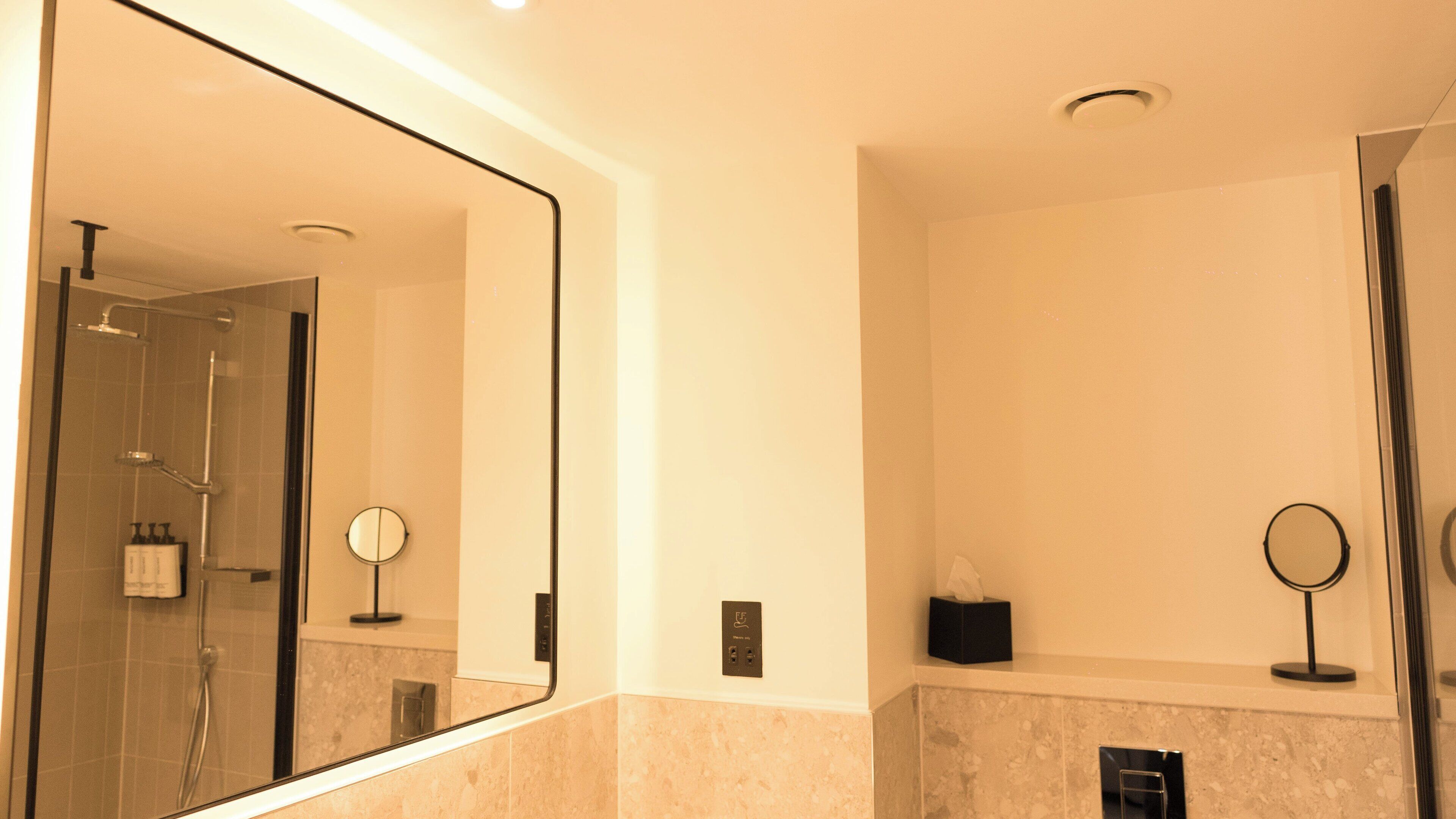 A modern bathroom with a large mirror, a shower, and a vanity with a towel dispenser.