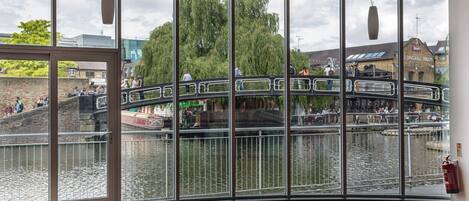 A panoramic view of a riverside area with a pedestrian bridge, a river, and buildings in the background.
