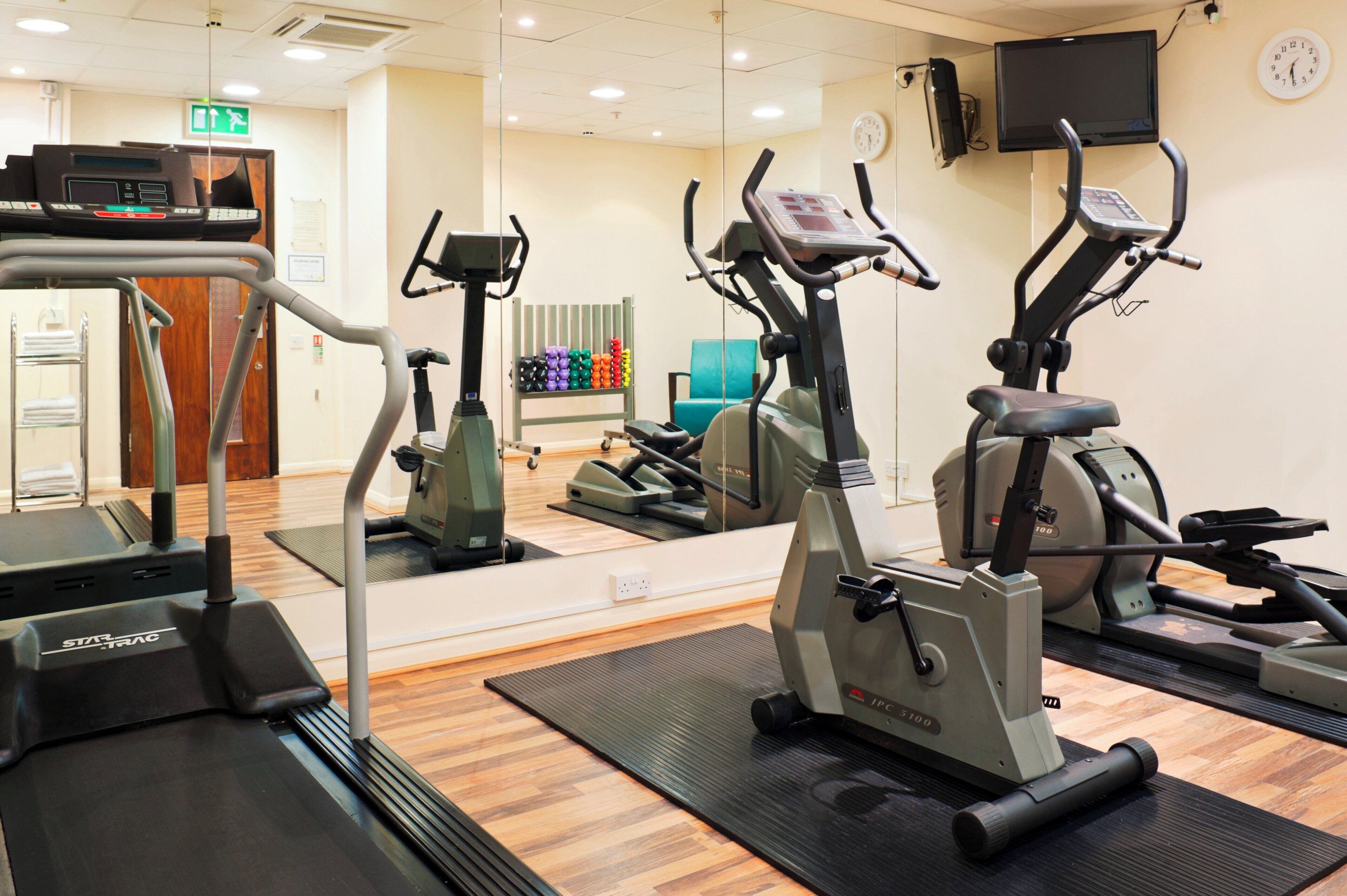 Une salle de sport équipée de divers appareils d’exercice, notamment des tapis de course et des vélos d’appartement, et dotée d’un mur recouvert de miroirs qui reflète les appareils.