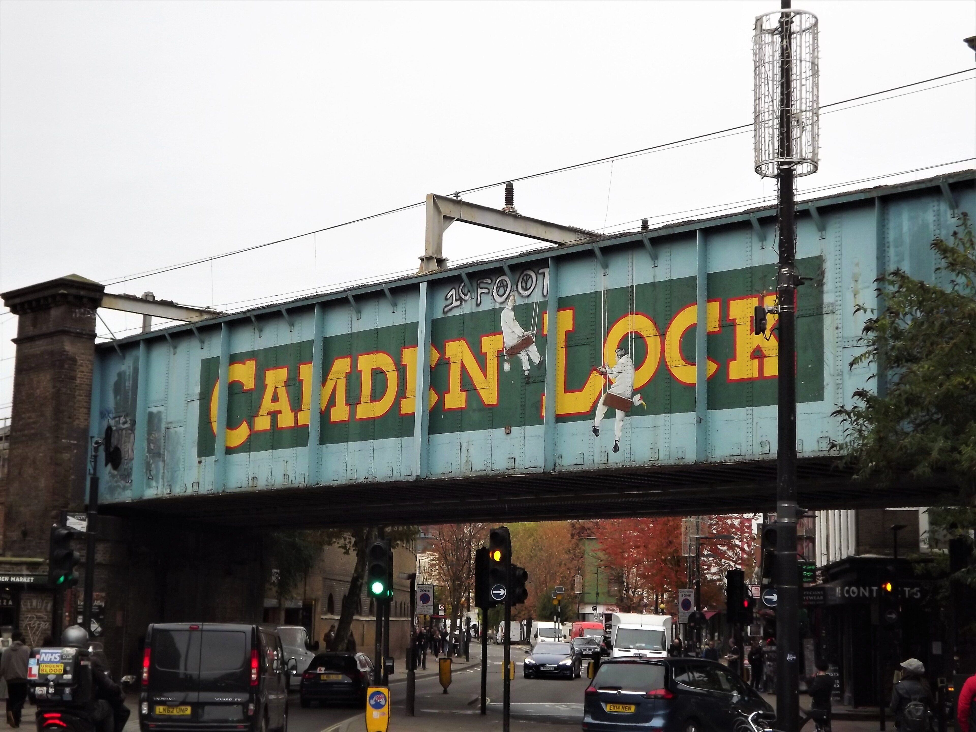 A bridge with the text 'CAMDIN LOCK' and a street scene below with traffic lights and vehicles.