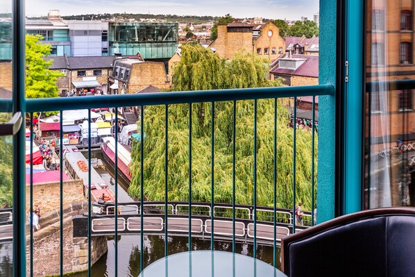 A view from a balcony with a metal railing, overlooking a canal with boats, a bridge, and a town with buildings and trees. - Holiday Inn London Camden Lock by IHG (London)