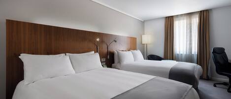 A hotel room with two beds, a desk, a chair, and a window with curtains.