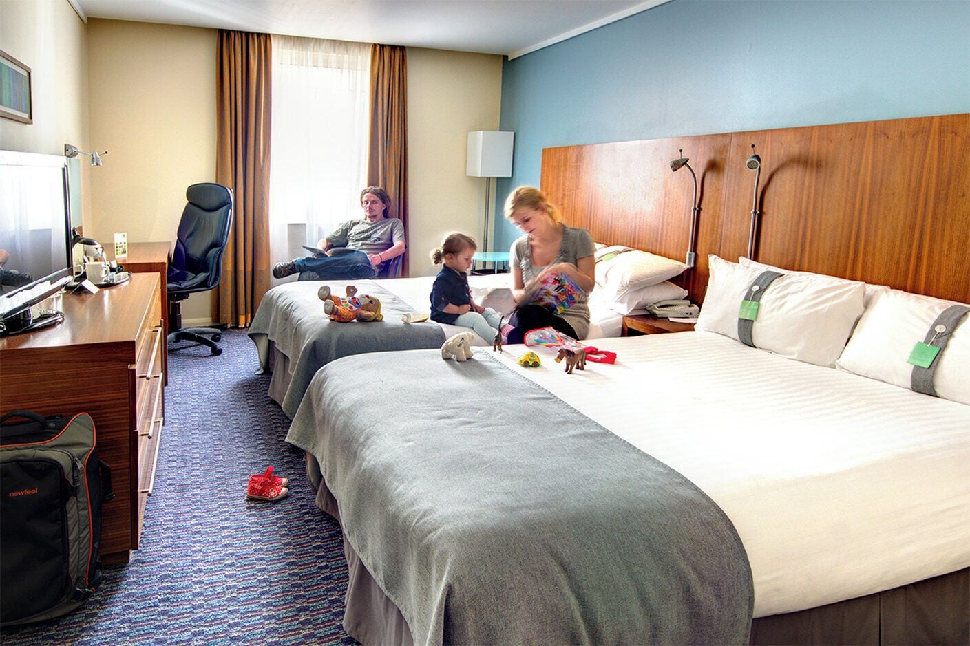 A hotel room with two beds, a desk, a chair, and a TV.