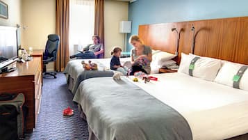 A hotel room with two beds, a desk, a chair, and a TV.
