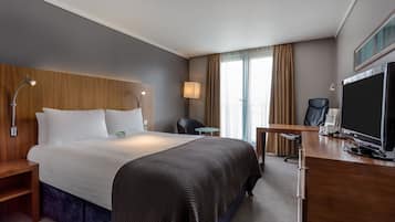 A hotel room with a large bed, a desk with a computer, a chair, and a TV.