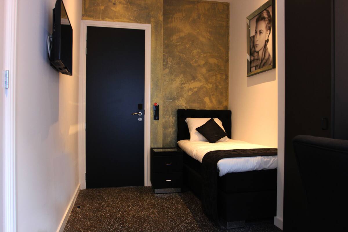 A bedroom with a bed, a nightstand, a TV mounted on the wall, and a door.