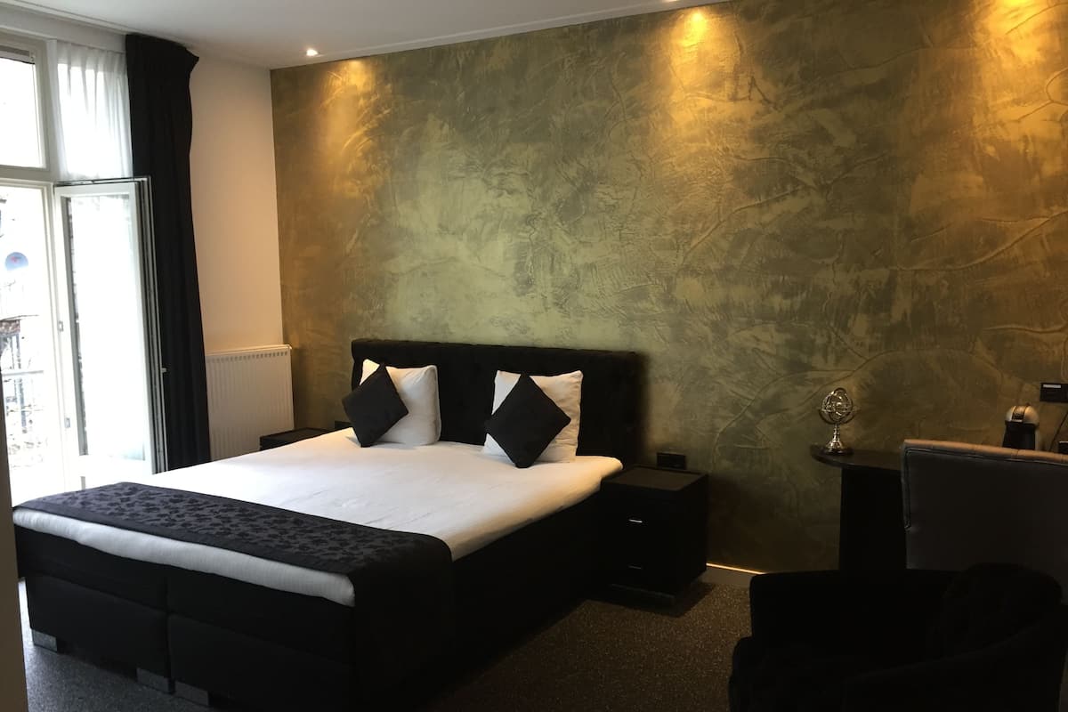 A modern hotel room with a large bed, a bedside table, a desk, and a chair.