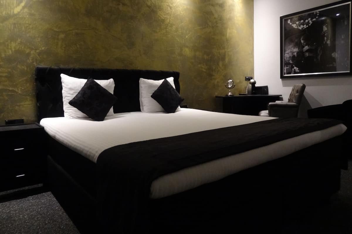 A modern bedroom with a large bed, a nightstand, a chair, and a wall-mounted artwork.