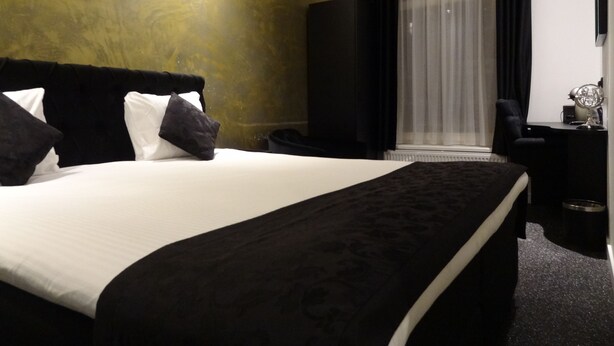 A hotel room with a large bed, a desk, a chair, and a large window with curtains. - Sara's Boutique Hotel (Amsterdam)