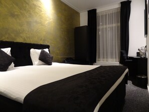 Une chambre d’hôtel avec un grand lit, un bureau, une chaise et une grande fenêtre avec des rideaux.