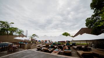 Un área de descanso al aire libre con sillones de sol y sombrillas, una piscina y un patio empedrado.