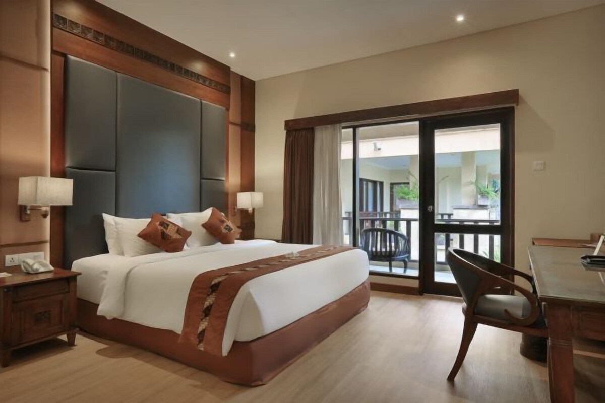 A hotel room with a large bed, a desk, and a balcony with a view.