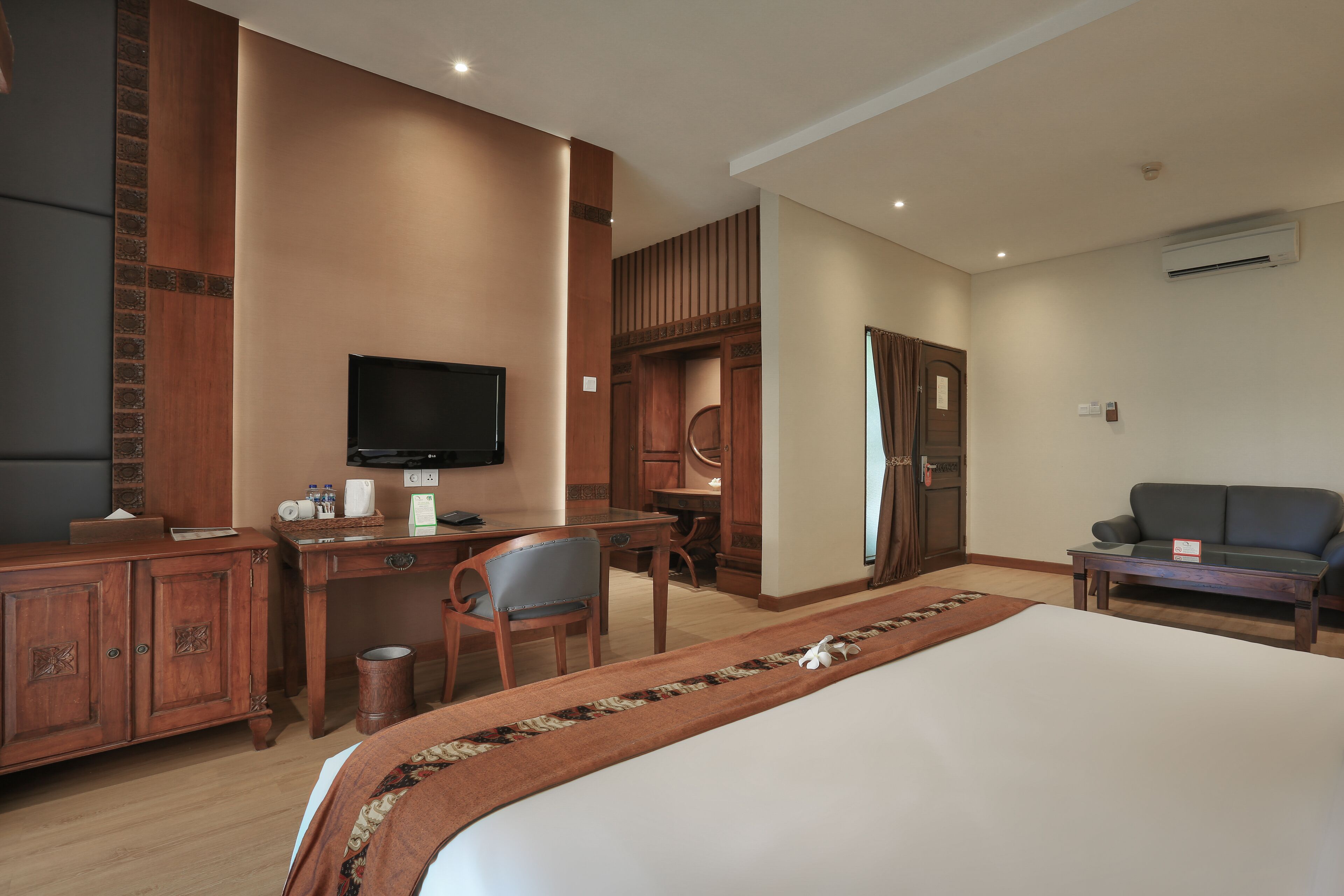A hotel room with a bed, a desk, a television, a wardrobe, and a sofa.