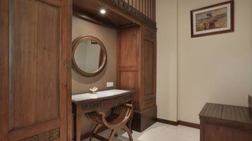 A wooden vanity with a mirror, a small table, and a chair in a room with a sloped ceiling and a framed picture on the wall.