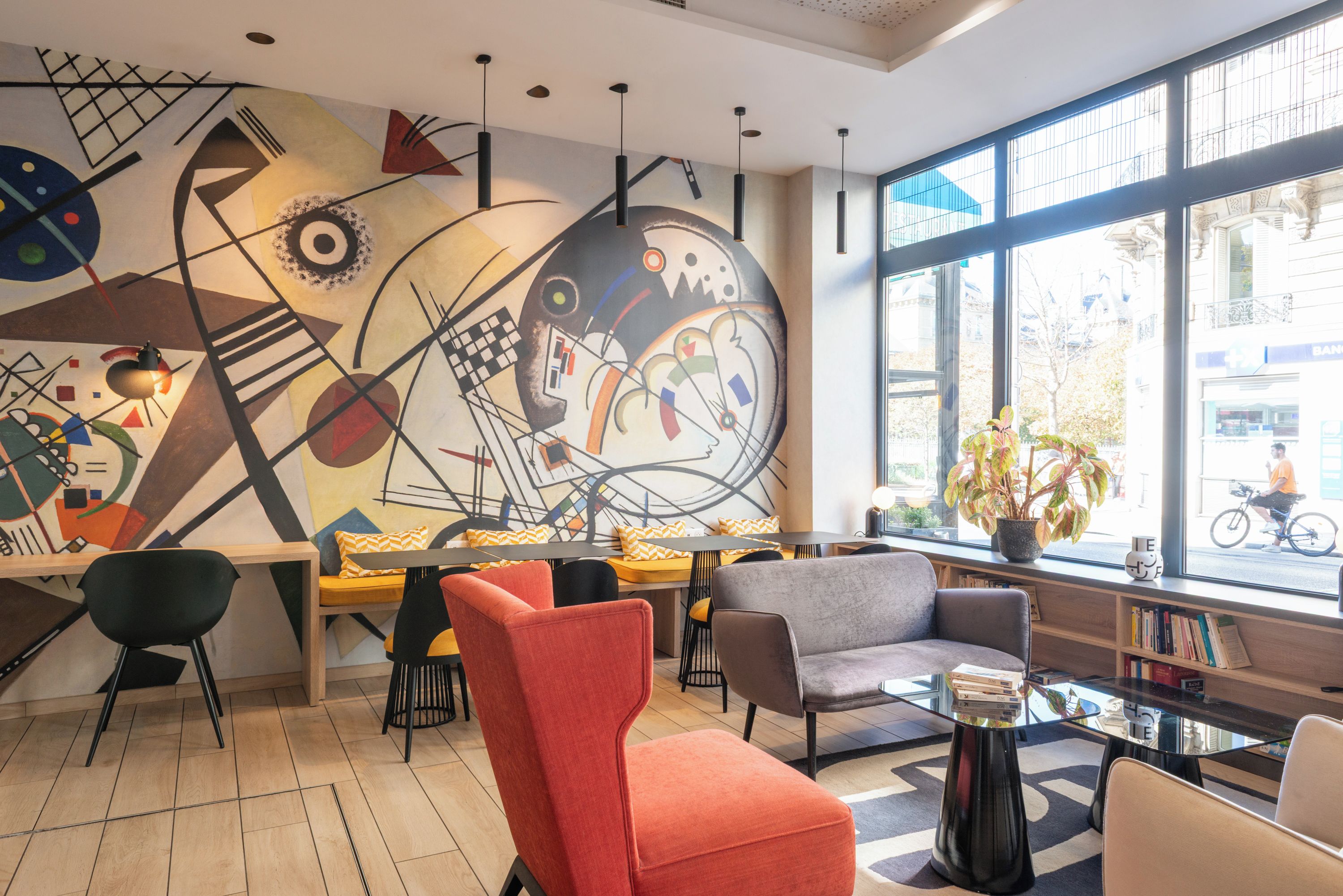 A modern interior with a large abstract mural, seating arrangements, and large windows offering a view of the street.