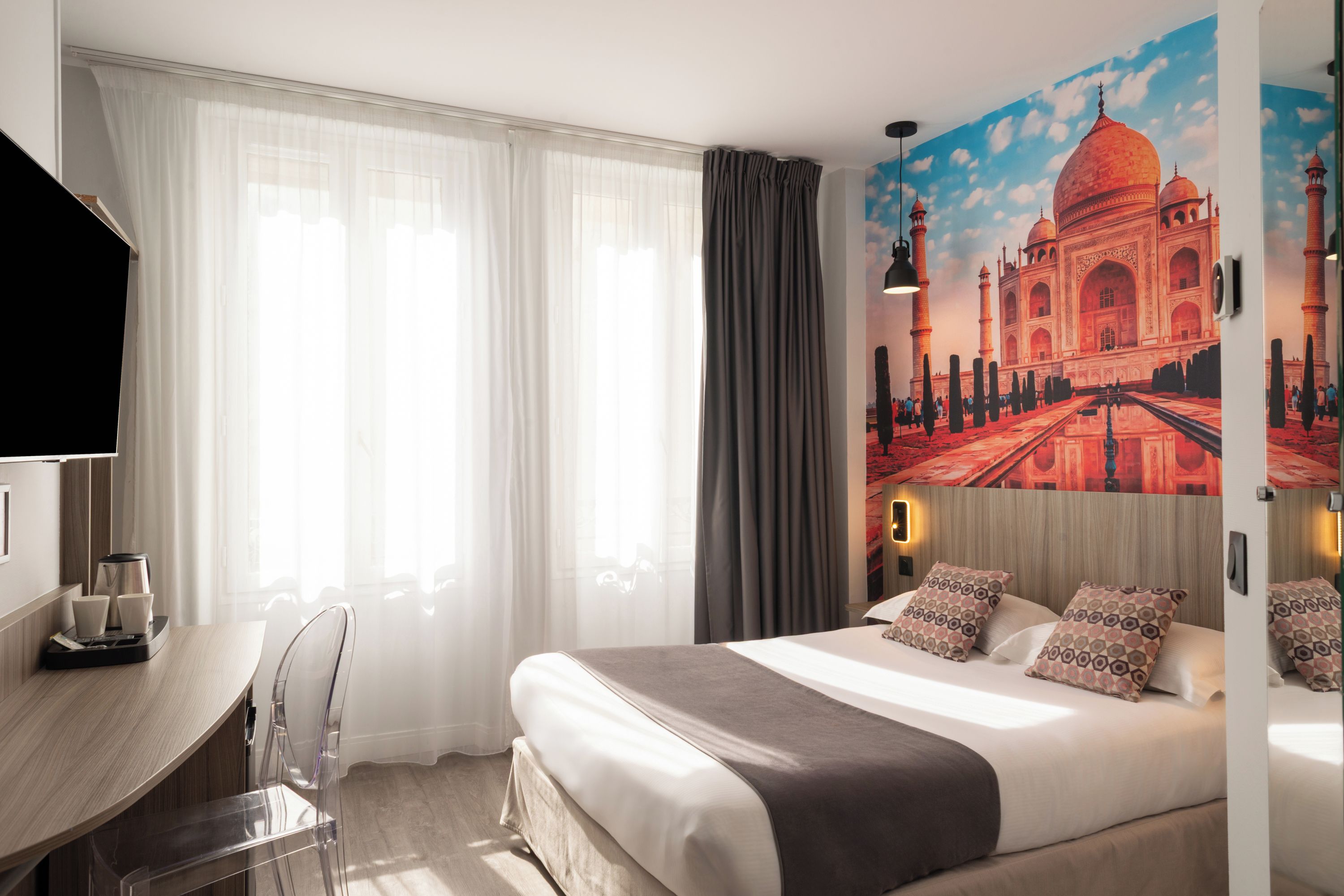 Une chambre d’hôtel comprenant un lit, un bureau, une chaise et une grande fresque murale représentant un bâtiment historique.