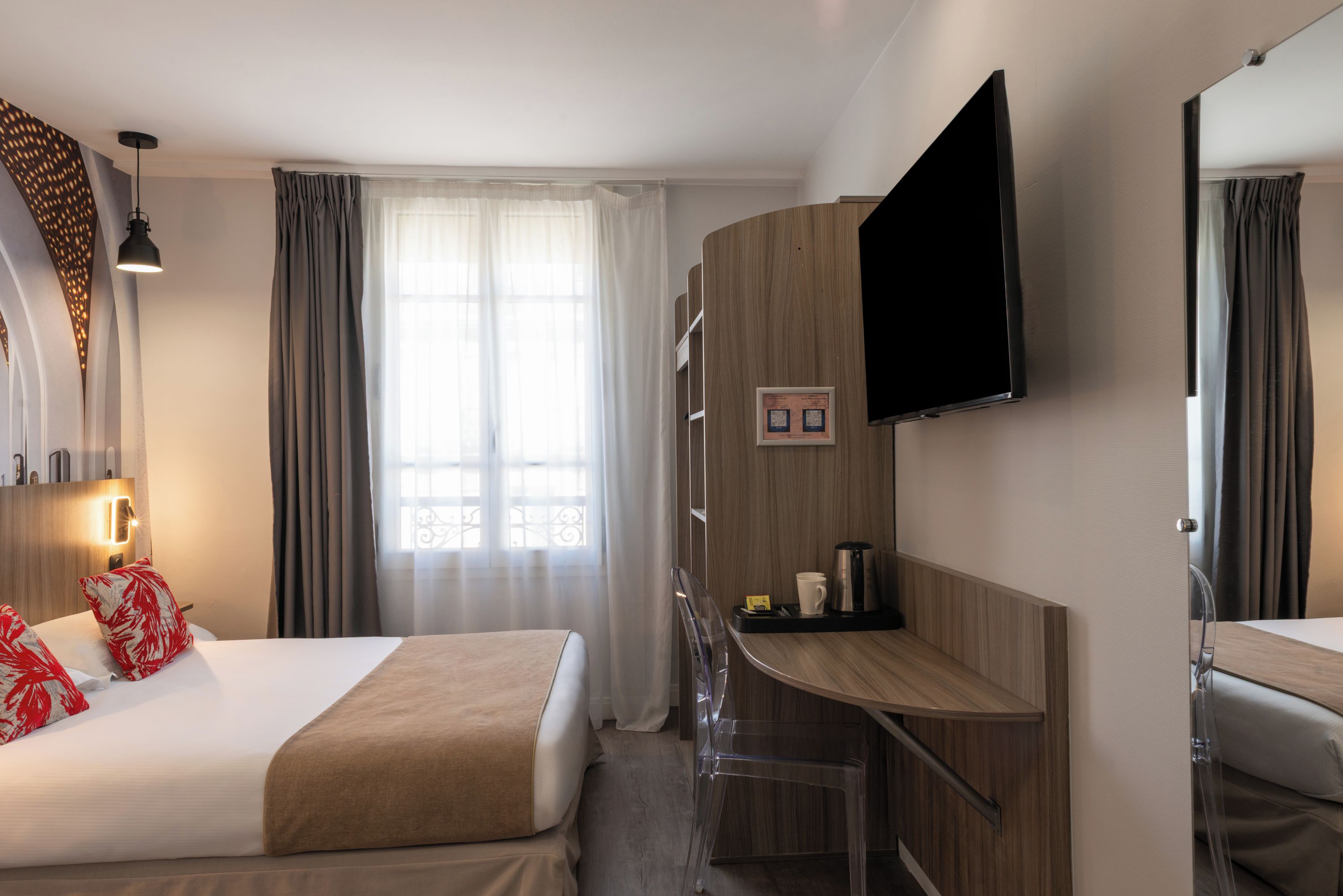 A hotel room with a bed, a desk, a chair, a flat-screen TV, and a window with curtains.