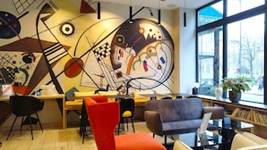 A modern interior with abstract wall art, a dining area, and large windows offering a view of the street. - Avia Saphir Montparnasse (Paris)