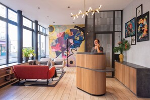 Un área de recepción con un mostrador de madera, un sofá rojo y un mural abstracto colorido en la pared.