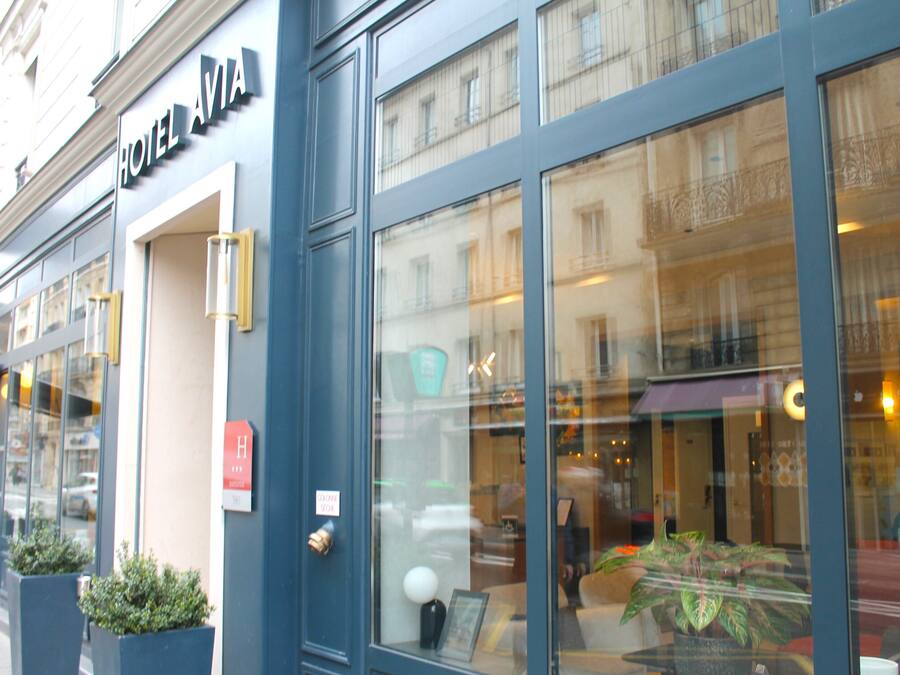 Fachada de hotel con amplios ventanales, un letrero que dice "HOTEL AVIA" y una puerta con un letrero con la letra "H" que indica una habitación accesible para personas con discapacidad.