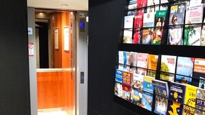 A hallway with a wall-mounted display of various travel posters and a wooden elevator. - Avia Saphir Montparnasse (Paris)