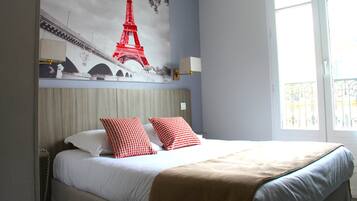 Una habitación de hotel con una cama, un mural grande de la Torre Eiffel, una ventana con vistas y una lámpara de noche.