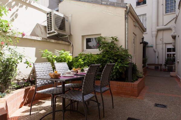 A small outdoor dining area with a table and chairs, surrounded by potted plants and a brick wall.