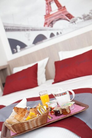 A breakfast tray with croissants, jams, honey, and orange juice on a bed with red pillows and a view of the Eiffel Tower. - Hôtel Saphir Grenelle (Paris)