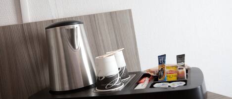 Een koffiezetapparaat, twee papieren bekers en een theedispenser op een zwarte dienblad.