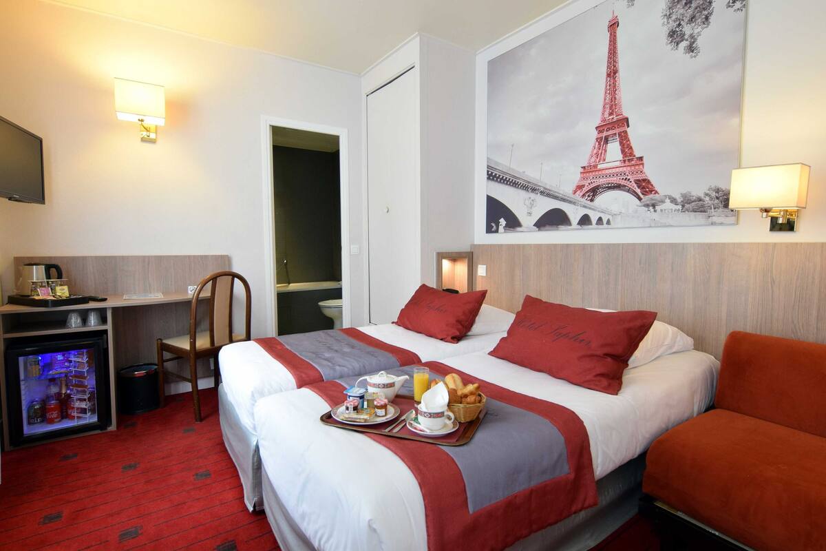 Habitación de hotel con dos camas, un escritorio, un refrigerador y un televisor montado en la pared.