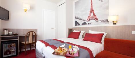 A hotel room with a bed, a desk, a chair, a refrigerator, and a wall with a picture of the Eiffel Tower.
