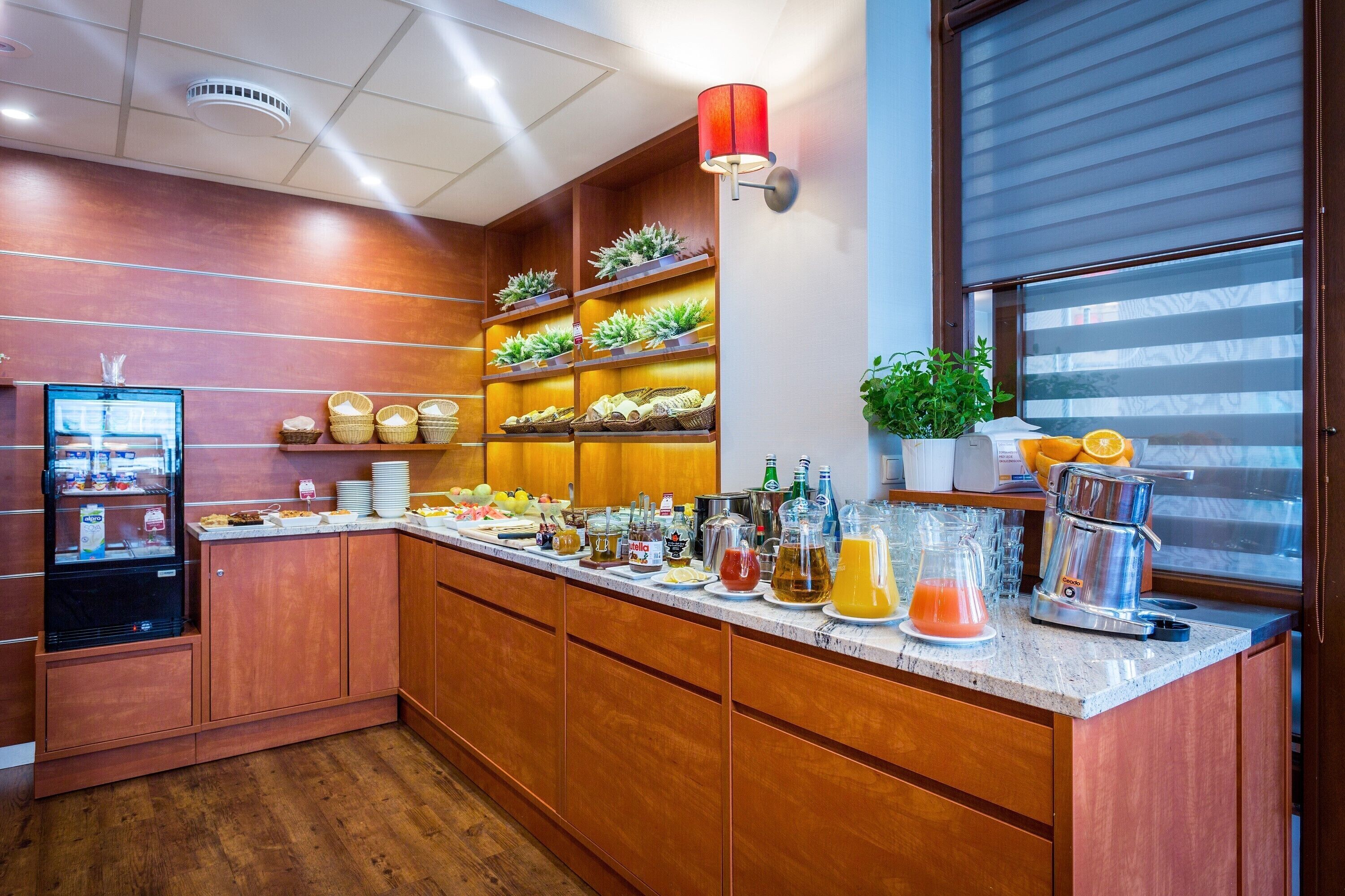 A kitchen area with wooden cabinets, a refrigerator, a coffee machine, and various food items on the counter.